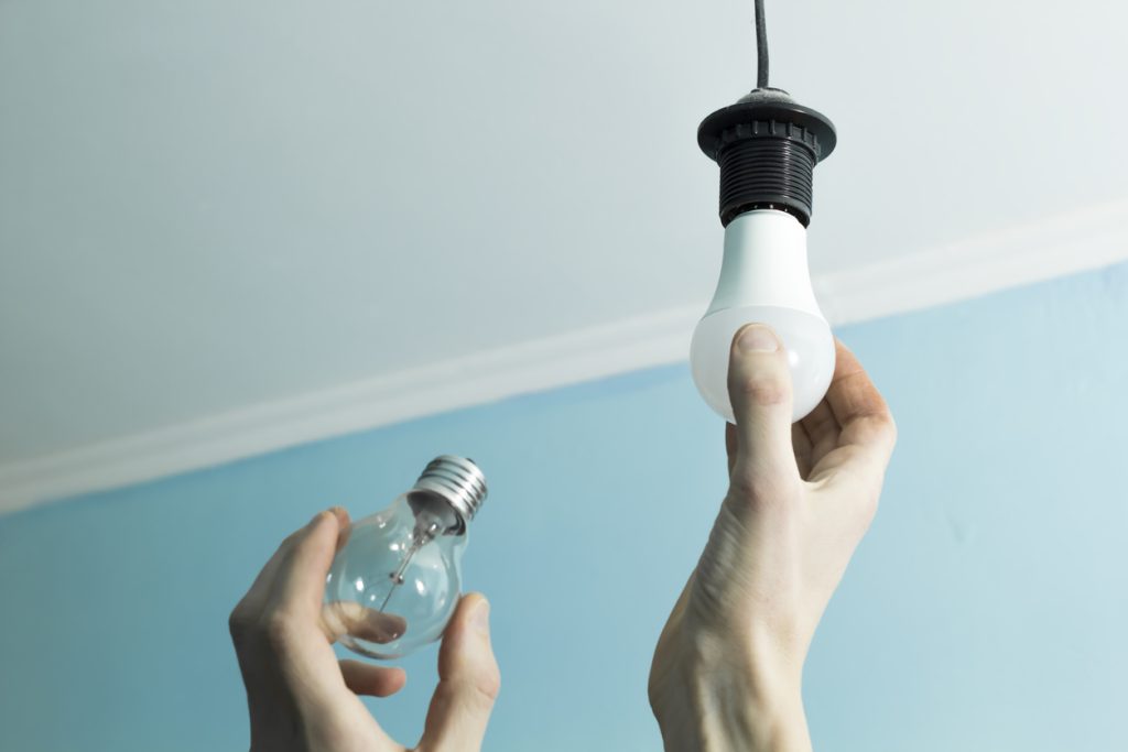 Incandescent lamp is changed to LED light by the hands of a man. Energy saving.